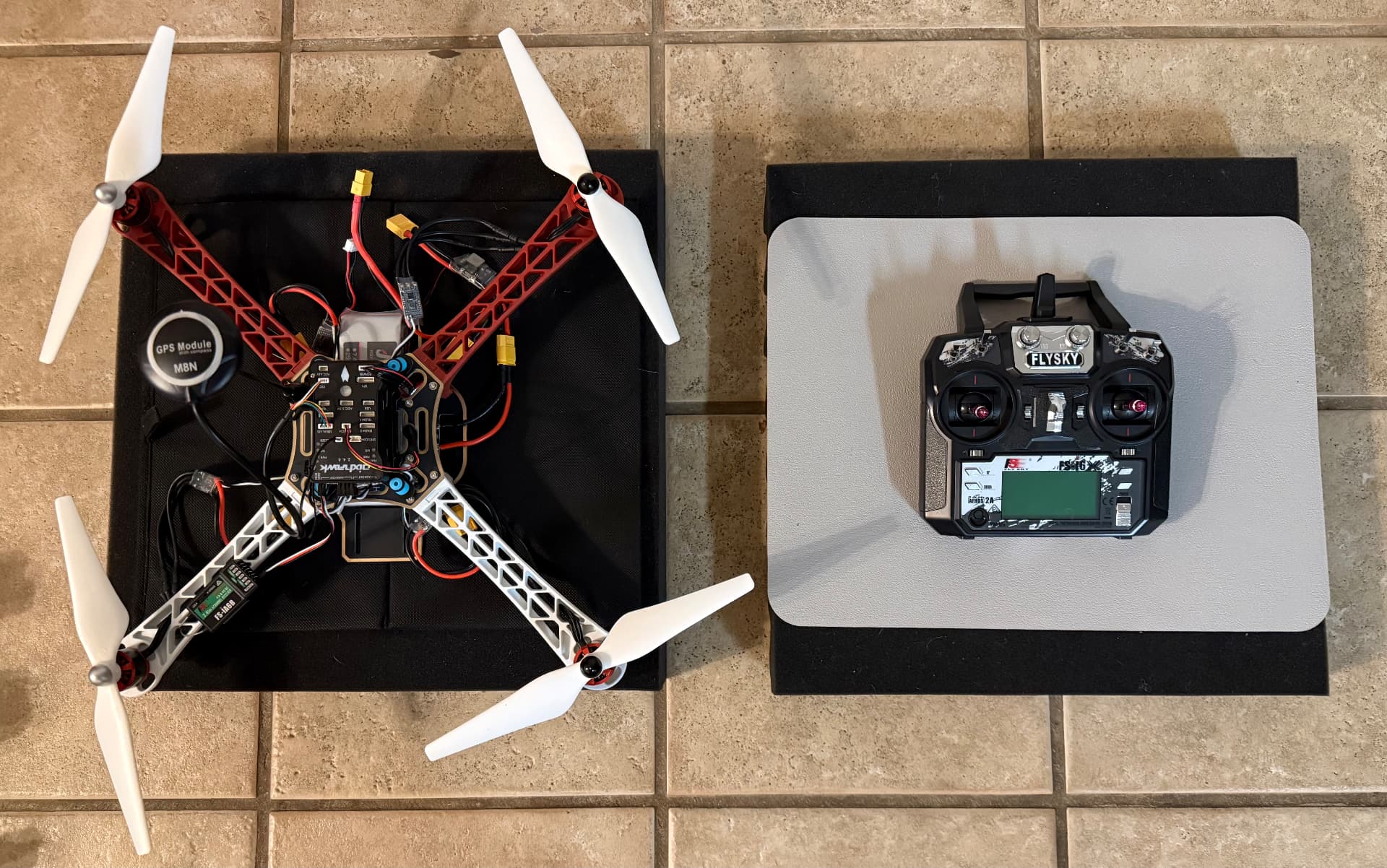 Built HAWK'S WORK F450 quadcopter with red and white arms, Pixhawk flight controller, M8N GPS module, and FS-iA6B receiver, next to its FlySky FS-i6X transmitter