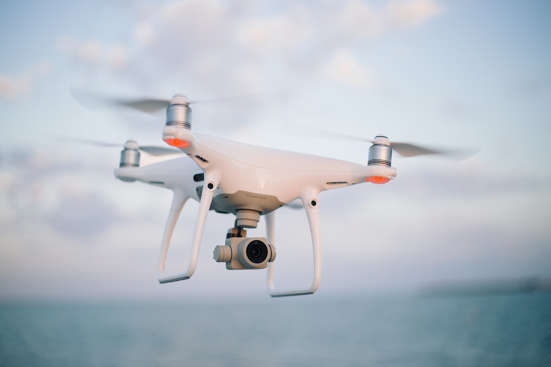 White camera quadcopter hovering over water with a gimbal-mounted camera underneath